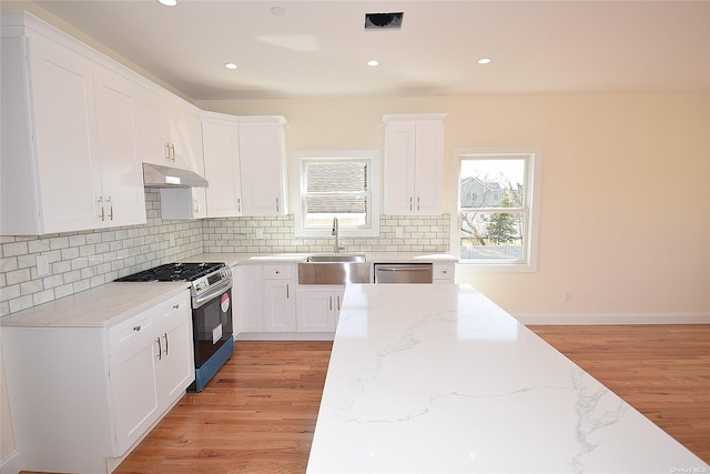 kitchen with white cabinets, stainless steel appliances, light stone counters, and light hardwood / wood-style flooring