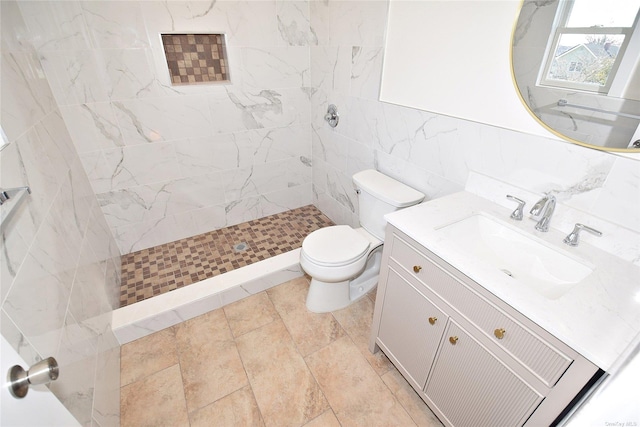 bathroom with a tile shower, vanity, toilet, and tile walls