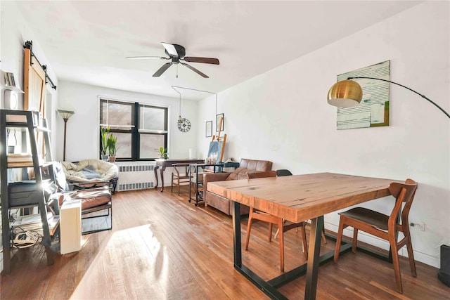 dining room with a barn door, ceiling fan, hardwood / wood-style floors, and radiator