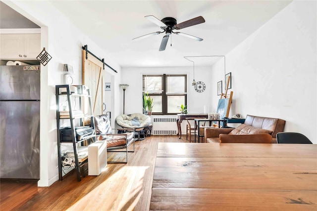 living room with a barn door, ceiling fan, radiator heating unit, and wood-type flooring