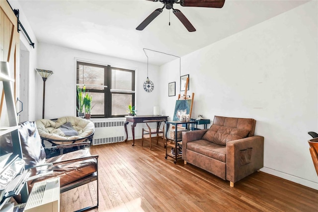 living area featuring a barn door, hardwood / wood-style flooring, radiator, and ceiling fan