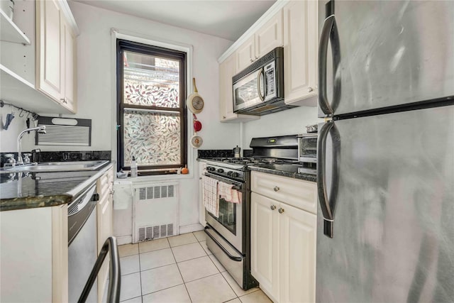 kitchen with radiator, dark stone counters, stainless steel appliances, sink, and light tile patterned flooring