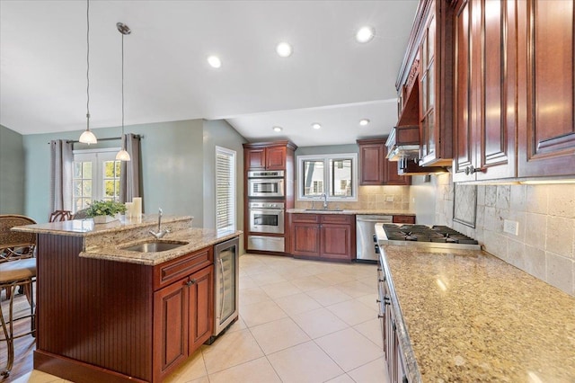 kitchen with appliances with stainless steel finishes, a breakfast bar, sink, a center island with sink, and hanging light fixtures