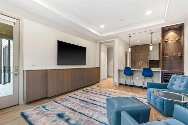 living room featuring light hardwood / wood-style floors, a raised ceiling, sink, and a wealth of natural light