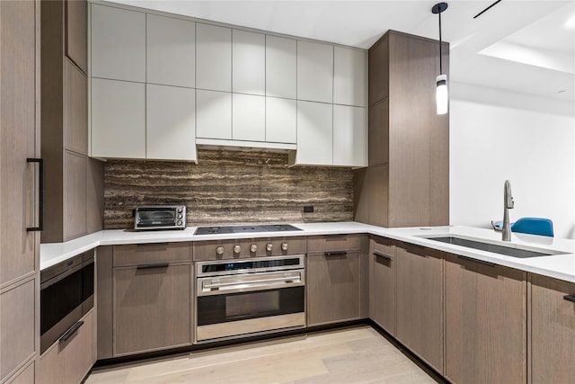 kitchen with backsplash, stainless steel oven, black electric cooktop, sink, and hanging light fixtures