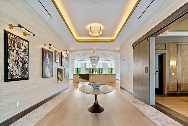 corridor featuring a raised ceiling, a chandelier, and light hardwood / wood-style floors