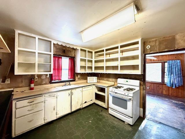 kitchen with white cabinets, white range with gas stovetop, sink, and wooden walls