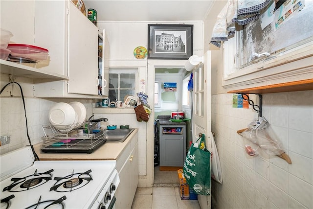 kitchen with white cabinets, light tile patterned floors, white stove, and sink