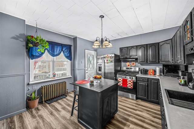 kitchen featuring radiator heating unit, a center island, stainless steel appliances, a notable chandelier, and hardwood / wood-style floors