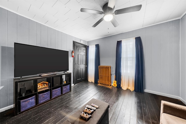 unfurnished living room featuring dark hardwood / wood-style floors, radiator, wooden walls, and ceiling fan