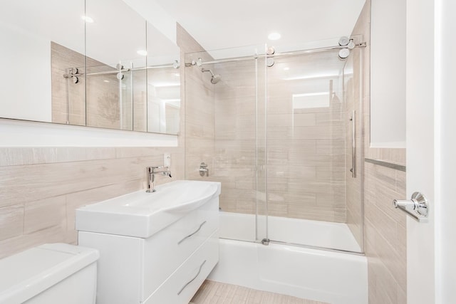 full bathroom featuring vanity, toilet, tile walls, and combined bath / shower with glass door