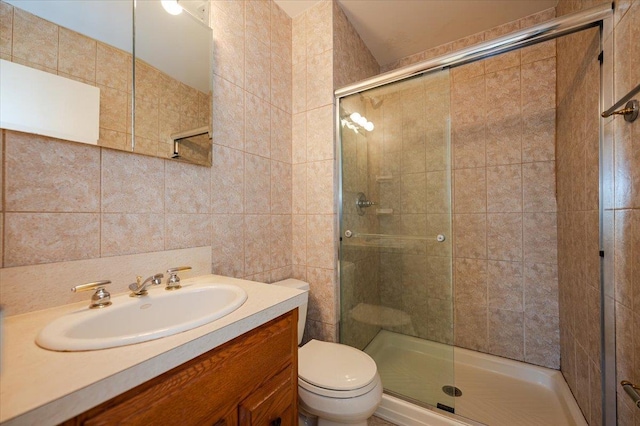 bathroom featuring toilet, vanity, tile walls, and a shower with shower door