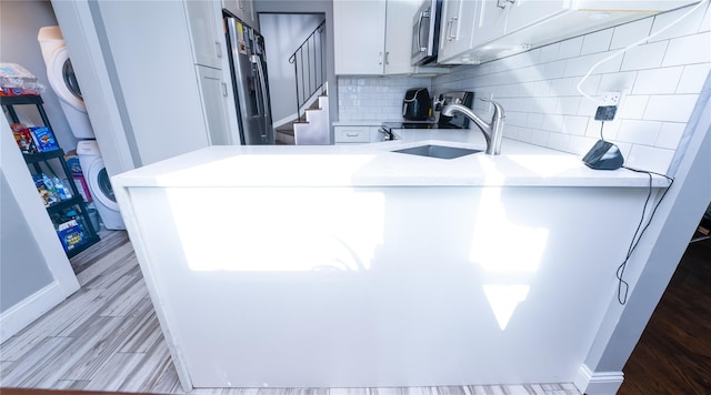 kitchen with sink, tasteful backsplash, kitchen peninsula, white cabinets, and stacked washer and clothes dryer