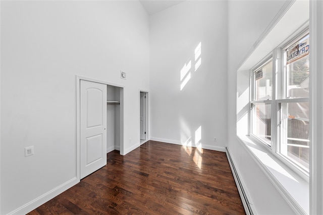 unfurnished room with dark hardwood / wood-style flooring, a towering ceiling, and a baseboard radiator