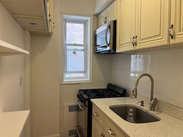 kitchen featuring light stone countertops, sink, backsplash, cream cabinetry, and appliances with stainless steel finishes