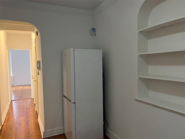 kitchen with built in features, white fridge, wood-type flooring, and ornamental molding