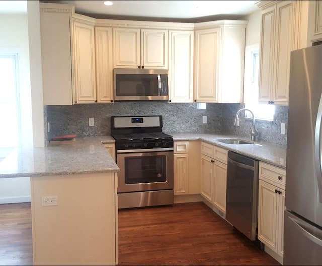 kitchen featuring kitchen peninsula, light stone countertops, appliances with stainless steel finishes, cream cabinetry, and dark hardwood / wood-style flooring