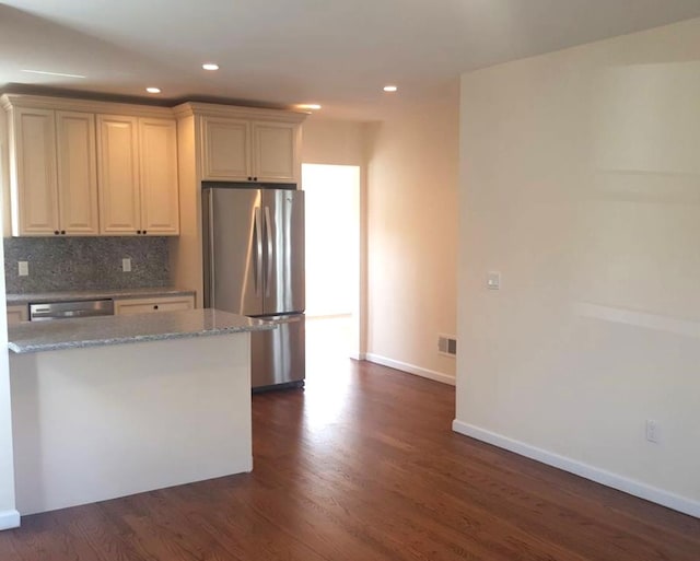 kitchen featuring tasteful backsplash, light stone countertops, appliances with stainless steel finishes, dark wood-type flooring, and cream cabinets