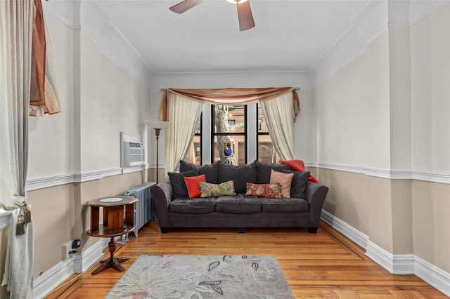 living room with light wood-type flooring, ornamental molding, ceiling fan, an AC wall unit, and radiator heating unit