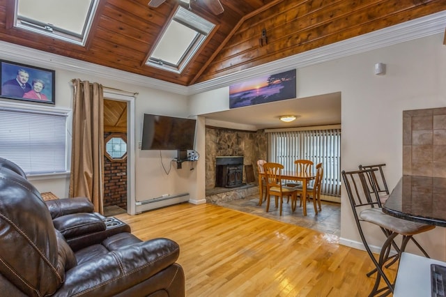 living room with a stone fireplace, light wood-type flooring, vaulted ceiling with skylight, and baseboard heating