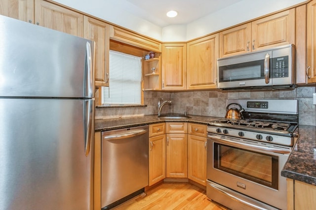 kitchen with sink, light hardwood / wood-style flooring, appliances with stainless steel finishes, dark stone counters, and decorative backsplash