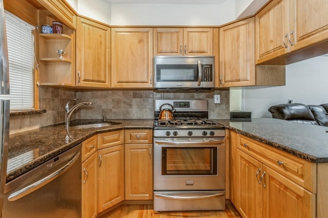 kitchen with sink, light wood-type flooring, dark stone counters, stainless steel appliances, and backsplash