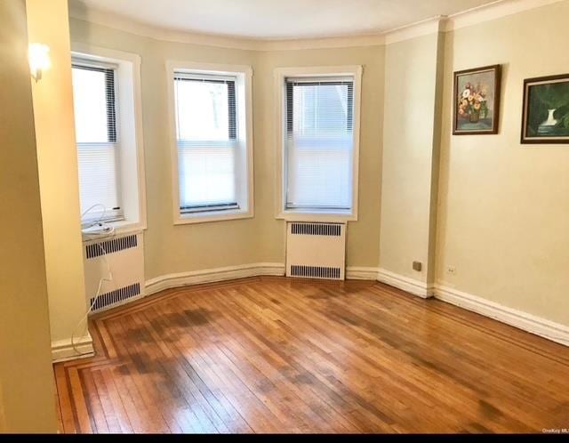 spare room with crown molding, radiator heating unit, and hardwood / wood-style floors