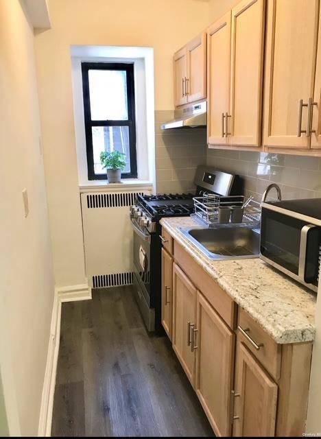 kitchen featuring radiator, stainless steel gas stove, dark wood-type flooring, decorative backsplash, and light brown cabinetry