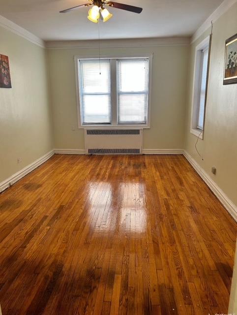 empty room featuring radiator heating unit, ceiling fan, crown molding, and wood-type flooring