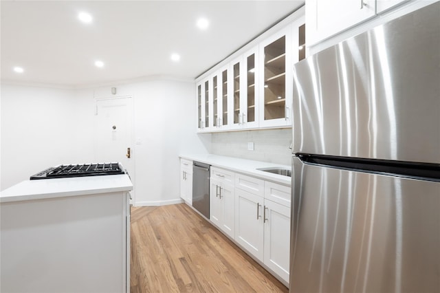 kitchen featuring appliances with stainless steel finishes, tasteful backsplash, white cabinets, crown molding, and light wood-type flooring