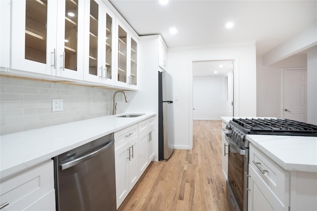 kitchen with sink, appliances with stainless steel finishes, white cabinetry, light stone countertops, and decorative backsplash