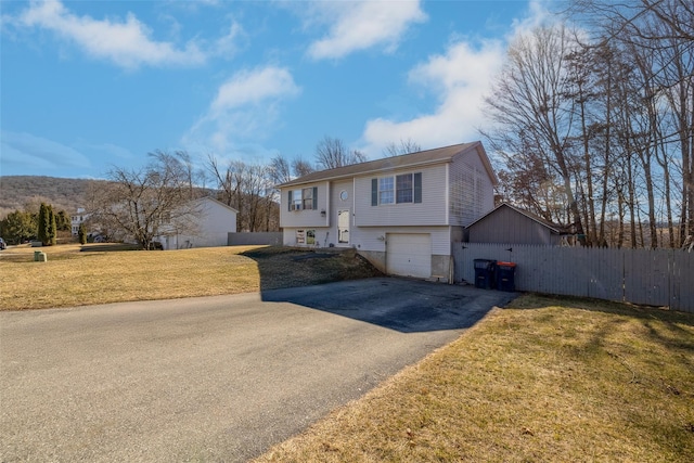 bi-level home with a front yard, an attached garage, driveway, and fence