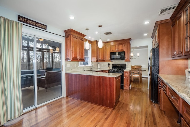 kitchen with sink, kitchen peninsula, decorative light fixtures, black appliances, and light wood-type flooring