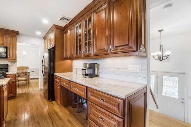 kitchen featuring light stone counters, black appliances, light hardwood / wood-style flooring, a notable chandelier, and hanging light fixtures