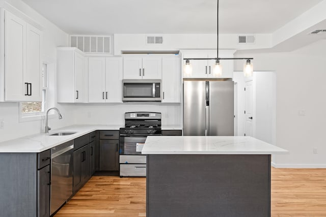 kitchen with a center island, white cabinets, sink, appliances with stainless steel finishes, and decorative light fixtures