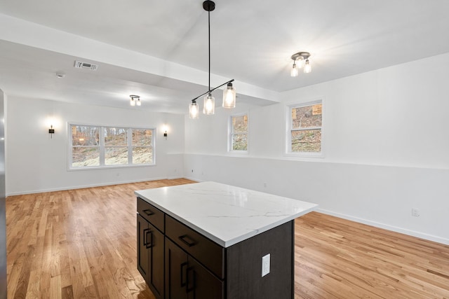 kitchen featuring dark brown cabinetry, light stone countertops, a center island, pendant lighting, and light wood-type flooring