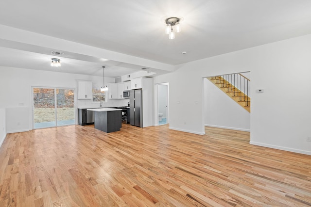 kitchen with stainless steel appliances, decorative light fixtures, a center island, light hardwood / wood-style floors, and white cabinetry