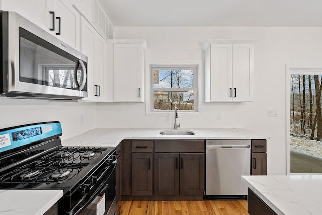 kitchen with white cabinets, sink, light wood-type flooring, light stone countertops, and appliances with stainless steel finishes