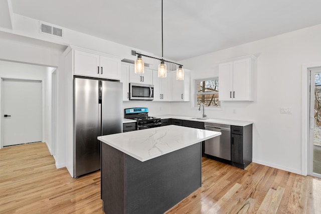 kitchen with white cabinetry, sink, stainless steel appliances, decorative light fixtures, and a kitchen island