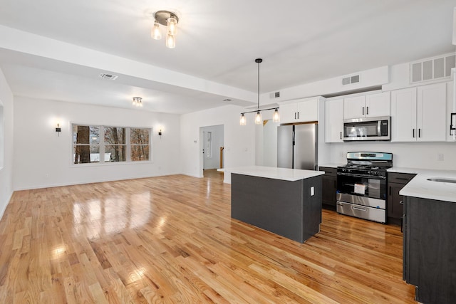 kitchen with stainless steel appliances, decorative light fixtures, light hardwood / wood-style flooring, white cabinets, and a kitchen island