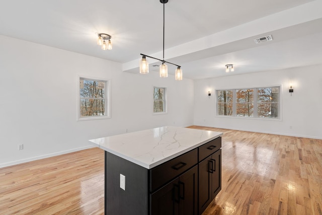 kitchen with a kitchen island, light stone countertops, light wood-type flooring, and hanging light fixtures