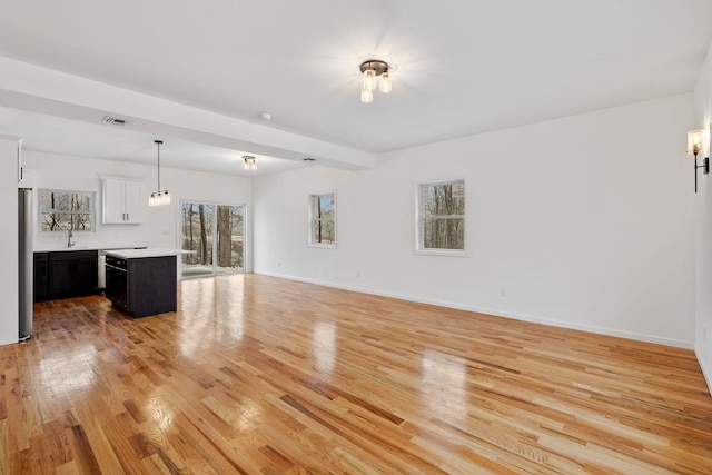 unfurnished living room with beam ceiling and light wood-type flooring