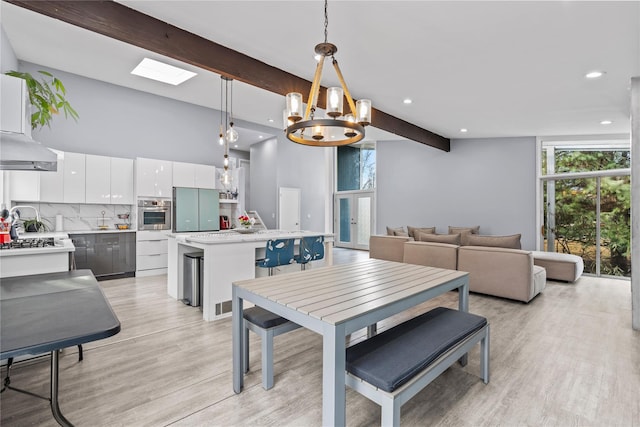 dining space with lofted ceiling with skylight, light wood-type flooring, and a chandelier