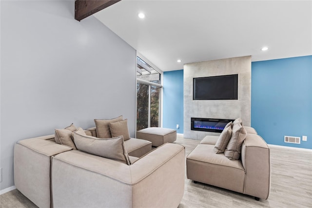 living room featuring vaulted ceiling with beams, light hardwood / wood-style floors, and a fireplace