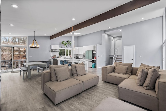 living room featuring beamed ceiling, light wood-type flooring, and a chandelier