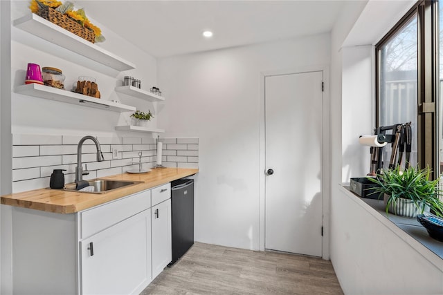 kitchen with wooden counters, decorative backsplash, sink, black dishwasher, and white cabinetry