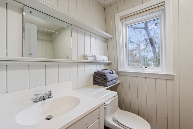 bathroom featuring vanity, toilet, and wood walls