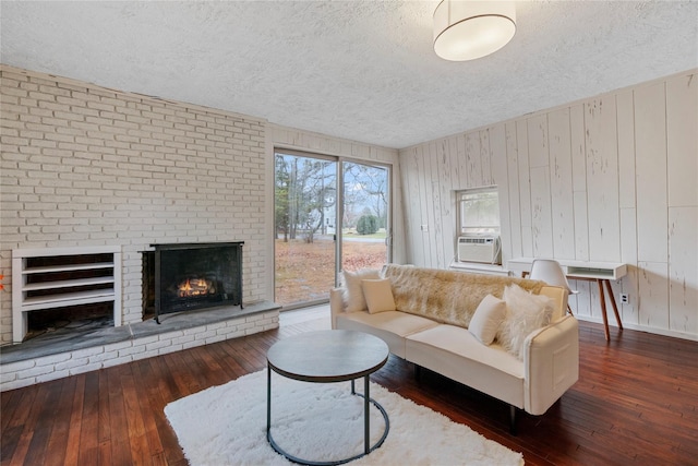 living room with wood walls, a fireplace, dark wood-type flooring, and a textured ceiling