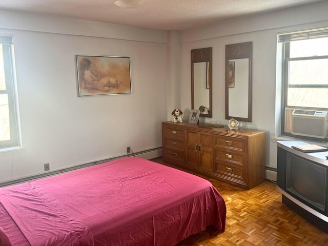 bedroom with parquet floors, a textured ceiling, baseboard heating, and cooling unit