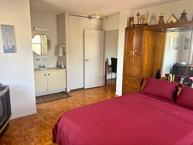 bedroom featuring connected bathroom, dark parquet flooring, sink, and a textured ceiling